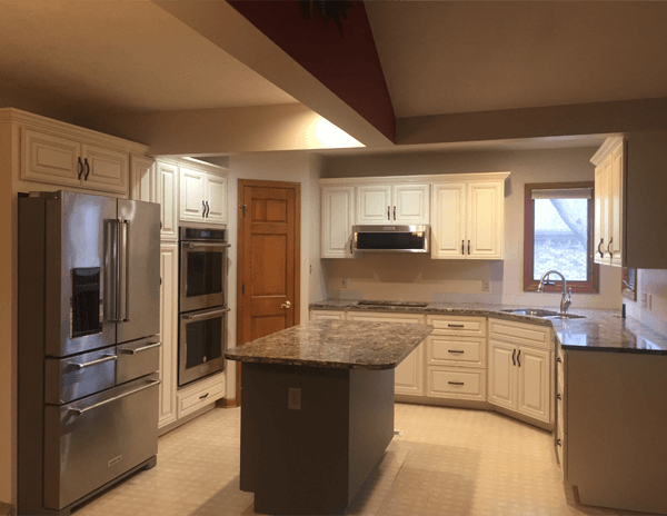 Cream refaced cabinetry with a granite island and stainless double ovens